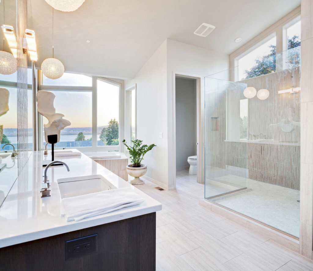 Modern bathroom remodel featuring large windows, a glass shower, double sinks, and a potted plant near the bathtub.